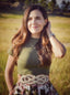 Image of Azomalli founder Paola, in a green shirt and floral skirt, standing in a golden field.